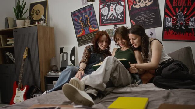 Caucasian teenage girls sitting on bed, reading book together, pointing at pages and laughing. Footage is ideal for youth education, student lifestyle, and peer learning commercial campaigns