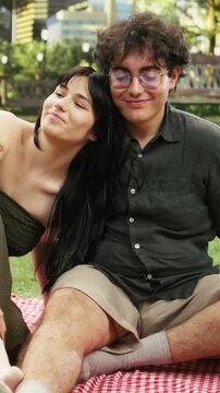 Vertical video: Romantic couple shares an intimate moment and kisses during a picnic date, showing love and affection on a blanket in a city park as boyfriend and girlfriend share a kiss and romance.