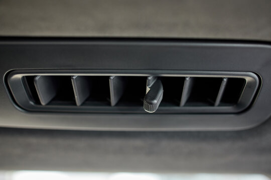 Close-up car interior roof air vent with hanging fragrance clip in black fabric headliner, showing glossy plastic slats, textured trim, centered cabin detail, soft overhead lighting