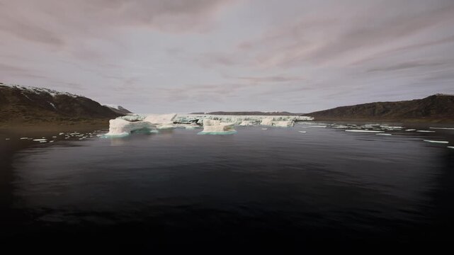 Icebergs drift serenely in the still waters of Greenland during twilight, reflecting shades of blue and gray. The surrounding landscape features rugged cliffs and a peaceful atmosphere.