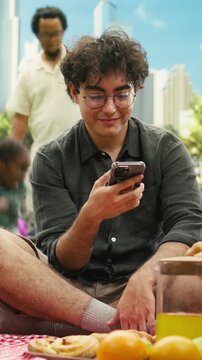 Vertical video: Disconnected couple scrolls through social media during picnic date, showing digital distraction, silence and disengagement between them.