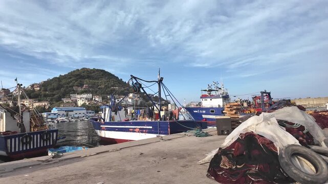 Blue and white fishing boat docked at harbor with piled nets on pier