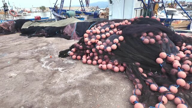 Large pile of black fishing nets with colored floats on harbor dock detailed