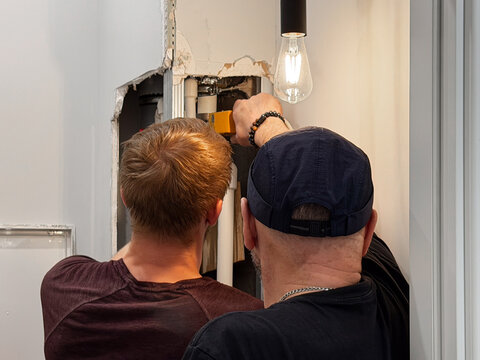 Two professional plumbers fixing water leak disaster by welding plastic polypropylene pipes inside damaged drywall wall opening, maintenance technician repairing leaking pipeline emergency. 