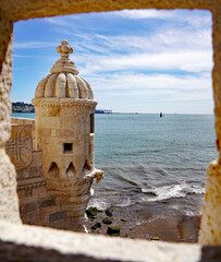 A stone bartizan turret of the historic Belém Tower overlooking the Tagus River is framed through a masonry opening under a bright blue sky in Lisbon, Portugal © Gregory