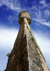 A dramatic low-angle perspective looks up the towering stone angle of the historic Cascais Citadel wall to a circular bartizan turret against a vivid blue sky in Cascais, Portugal © Gregory