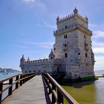 A wooden walkway leads directly toward the iconic Manueline limestone fortress of Bel&eacute;m Tower rising from the waters of the Tagus River in Lisbon, Portugal