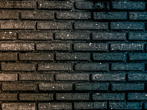 High-resolution texture of a dark brick wall featuring a creative lighting split, blending warm golden tones on the left with cool cyan and blue highlights on the right. 