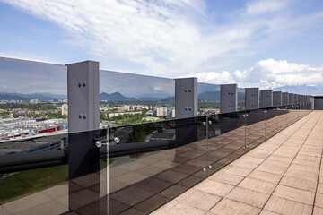 Fototapeta premium Modern rooftop balcony with glass protective barrier overlooking city and mountain landscape