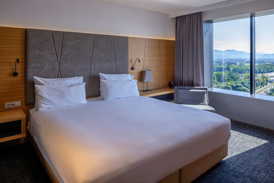 Elegant hotel bedroom with comfortable king bed panoramic window view and wooden headboard
