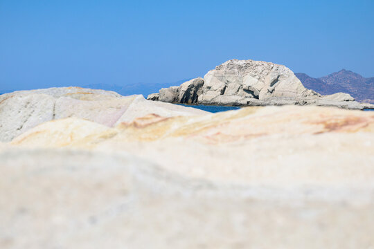 White coastal rock formations rise from the blue Aegean Sea near Mandrakia, Milos, Greece, under a bright summer sky.