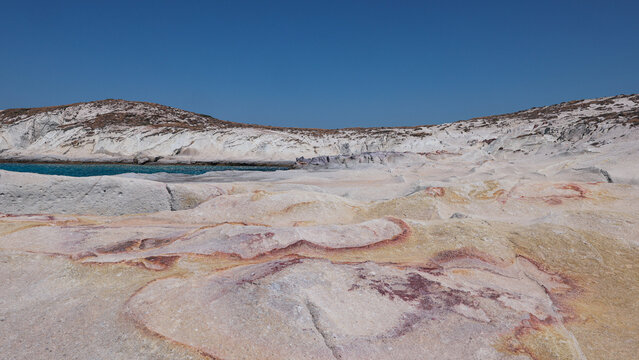 Sunlit rock formations display natural red and yellow mineral patterns near Mandrakia, Milos, Greece.