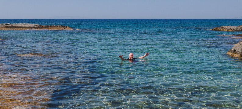 A swimmer enjoys the crystal‑clear turquoise water near Mandrakia, Milos, Greece, surrounded by rocky coastal scenery.