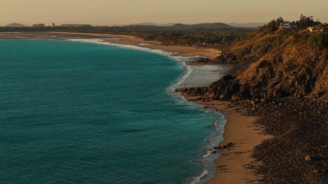 Aerial video along a tropical beach at dawn with golden sunrise over rocks