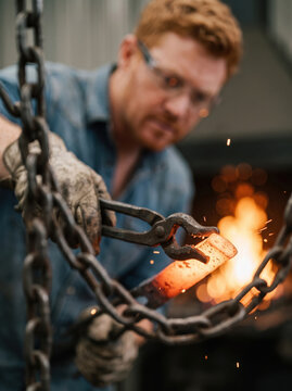 Blacksmith forging heated chain link in workshop