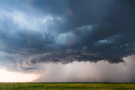 Low shelf cloud rolling across the sky with a wall of rain sweeping over a bright green field