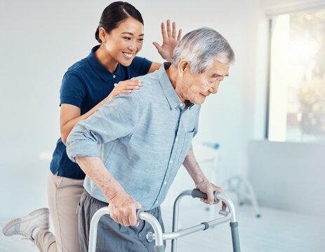 Japanese physiotherapist supporting an elderly man walking with an aluminium walking frame in a rehabilitation room
