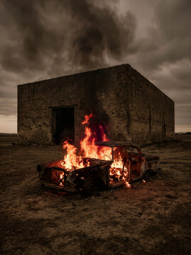 Burning car in front of abandoned building, apocalyptic scene with vintage car on fire and black smoke