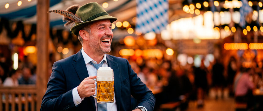 Smiling man in suit and traditional bavarian hat holding beer mug at Oktoberfest festival tent. Bavarian culture and german folk celebration concept. Autumn beer festival and tradition