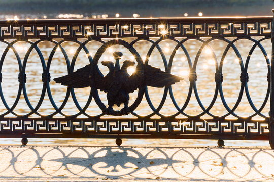 picturesque metal railings with a double-headed eagle and the crown of the Russian Empire on embankment in St. Petersburg, Russia, walking people, sunny autumn day, incredible sun glare Russia