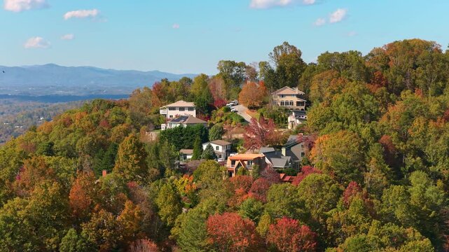 Aerial view of private homes nestled on colorful mountain hills near Asheville, North Carolina. Brilliant autumn foliage surrounds peaceful residential landscape.