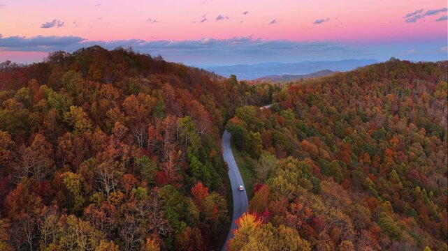 Car traveling on winding forest road in Tennessee Appalachians during fall season at sundown. Vehicle driving through mountain woods under glowing autumn leaves.