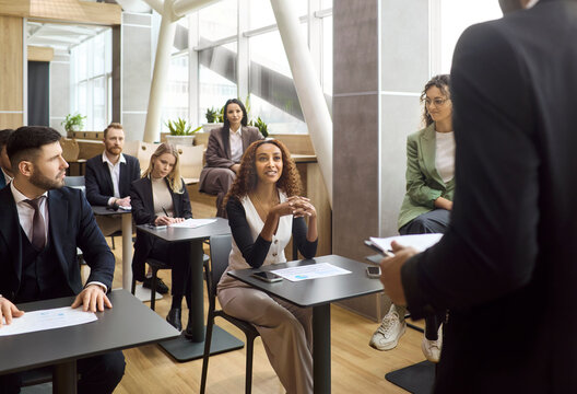 Team coworkers with coach in training meeting. Professionals listen to a speaker, ask questions and join discussion during a workshop in an office classroom. Clear teamwork and learning concept.