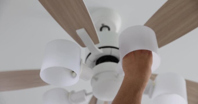 Man changing light bulb in ceiling fan at home, low angle view. Camera moving