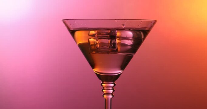 Ice cubes falling into martini glass with cocktail on color background, closeup