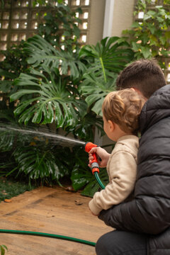 Toddler Boy and Father Watering a Small Backyard Garden Together