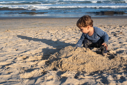Two-Year-Old Toddler Boy Playing in the Sand on a Sunny Beach on a Cool Day