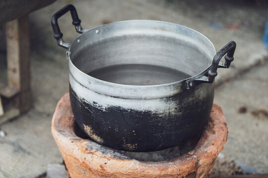 Vintage aluminum pot with soot on a traditional clay charcoal stove.An authentic high-quality shot of a classic Thai aluminum cooking pot filled with water.