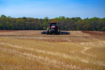 Fototapeta premium Tractor works under blue sky. Rural tractor handles ground preparation. Agricultural equipment keeps tractor on farmland. Spring landscape shows tractor with harrow.