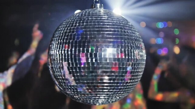 Shiny disco ball reflecting bright light in a dark club setting with blurry partygoers in the background