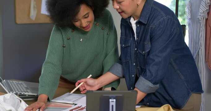 Camera starting close at table diverse women in green sweater denim shirt designing with swatches