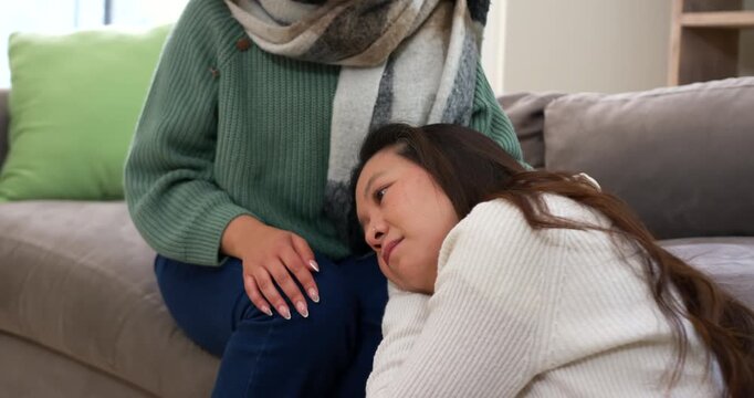 After upset cues, diverse women on sofa, one resting head on lap, other stroking hair, soothing