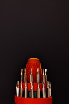 Multi bit screwdriver set showing variety of interchangeable metal heads in red plastic holder isolated on black background, Torx flathead and phillips heads for mechanical repair and DIY projects