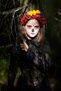 Halloween beauty portrait of woman in dark forest. Female face adorned with Santa Muerte makeup.