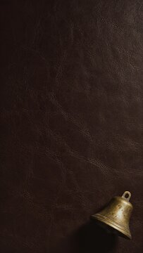 Vintage brass bell on dark brown leather background with rich texture and dramatic shadows. Perfect for holiday and rustic design projects.