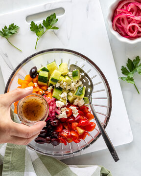 A hand about to pour dressing into a mediterranean salad before tossing.