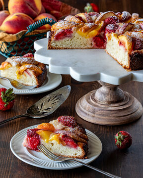 A pedestal stand with a homemade peach cake and one serving in front.
