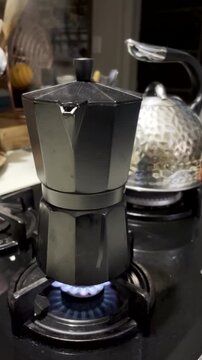 Vertical. Steam escapes spout of black bialetti heated on gas flame of hob