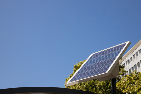 Solar panel stands tall against clear blue sky in urban environment. Renewable energy concept