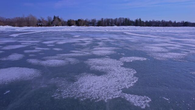View of intricate frozen lake, winter ice on body of water. Top down drone flight above ice formed crevasses and cracks. Cinematic aerial footage revealing ice formations patterns landscape.