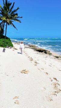 A mature woman is walking towards the camera on an empty beach in Oahu, Hawaii