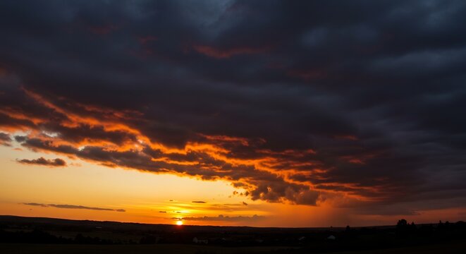 Dramatic Sunset Sky: The sun dips below the horizon, casting fiery orange and red hues across a dramatic sky filled with dark, brooding clouds, a stunning display of nature's power and beauty.