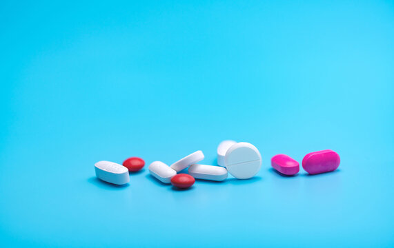 White and pink tablets pills on blue background. Pharmacy banner. Pharmaceutical industry. Health insurance strategy. Pharmaceutical manufacturing. Tablets pills production topics. Drug selection.