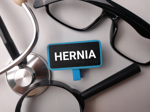 A small chalkboard clip showing HERNIA sits framed by a stethoscope, glasses, and a magnifying glass