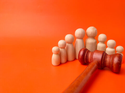 A wooden gavel lies in the foreground next to a line of wooden peg figures on orange