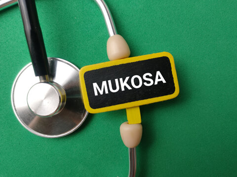 A small chalkboard clip displaying MUKOSA rests within the metal earpieces of a stethoscope on green